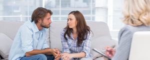 couple looking to each other during therapy session while therapist watches